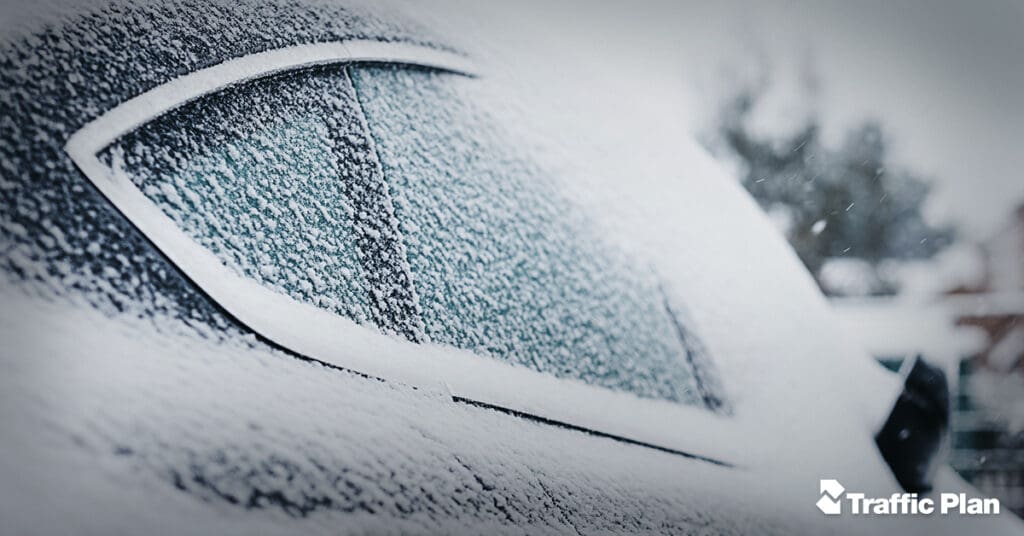 A car covered in snow, with a close-up of the rear window partially obscured by frost. The background is blurred, and the words Traffic Plan appear in the bottom right corner.