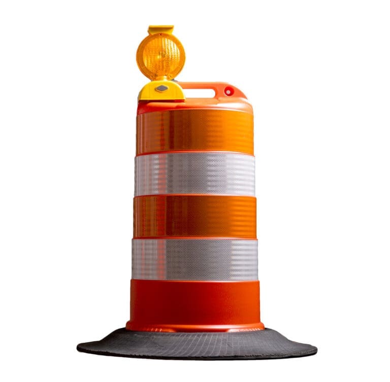 An orange and white striped traffic barrel with a reflective surface and a yellow warning light on top, placed on a black rubber base, isolated on a white background.