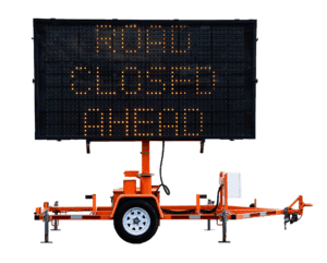 A portable electronic road sign displays the message ROAD CLOSED AHEAD in bright orange lights, mounted on an orange trailer with a single wheel, isolated on a white background.