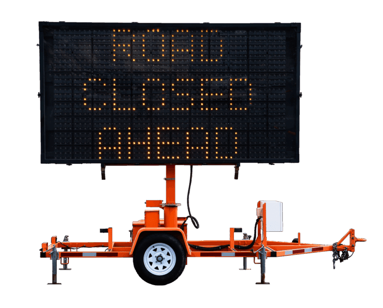 An electronic road sign mounted on a trailer displays the message “ROAD CLOSED AHEAD” in bright orange lights, indicating a road closure to upcoming traffic.