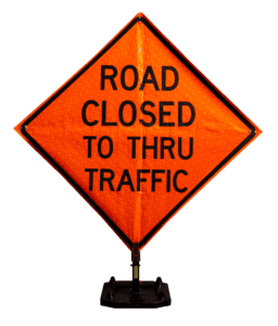 An orange diamond-shaped road sign with black text that reads, ROAD CLOSED TO THRU TRAFFIC, standing on a black base.