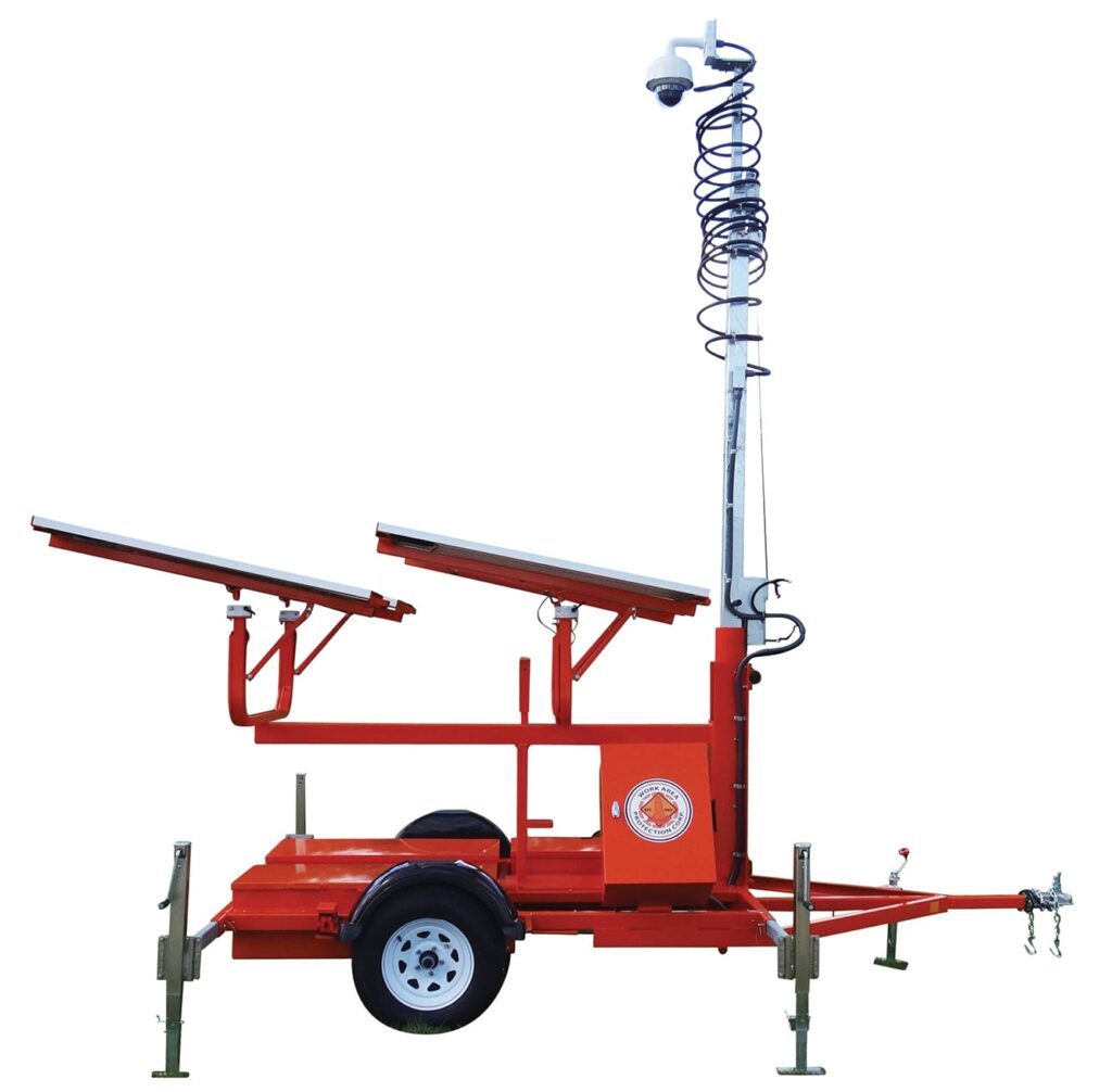 A red mobile security trailer with solar panels, a mounted camera on an extendable pole, four stabilizing legs, and a single axle with a wheel.