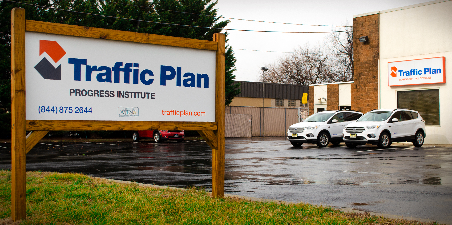 traffic plan progress institute sign sitting on green grass parallel to the company building with vehicle parked out front