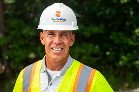 traffic plan employee posing in full company garb while standing in front of green bushes