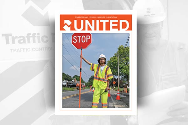 A construction worker in a reflective safety vest and helmet holds a stop sign on a street lined with traffic cones. The cover of United magazine is displayed over a faded background with the words Traffic Plan visible.
