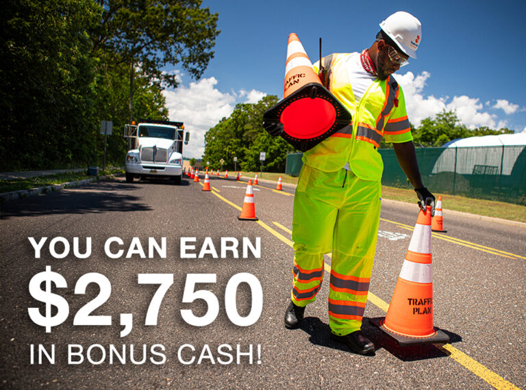 A man in a safety vest and hardhat carrying traffic cones.