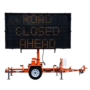A portable electronic road sign on a trailer displays the message ROAD CLOSED AHEAD in bright yellow lights.