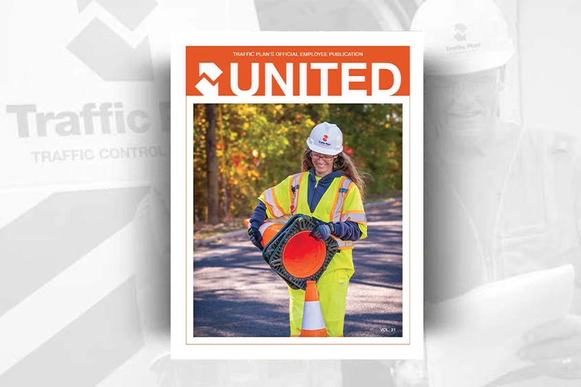 A woman in a safety vest and hard hat holds a traffic cone and sign on a road. The magazine cover reads UNITED in bold orange letters at the top.